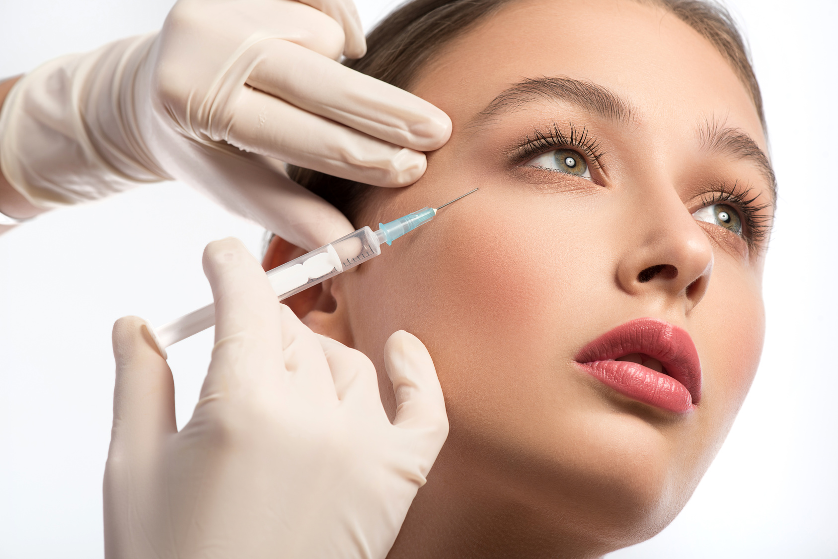 Serine young woman is getting facial botox injection. Beautician hands in gloves holding syringe near her face